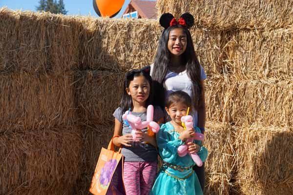 Three girls are standing next to each other in front of hay bales holding balloons.