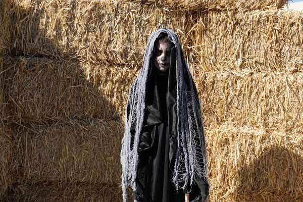 A person in a grim reaper costume is standing in front of hay bales.