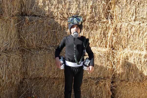 A young boy in a cat costume is standing in front of a hay bale.