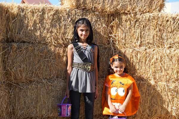 Two young girls in halloween costumes are standing next to each other in front of hay bales.