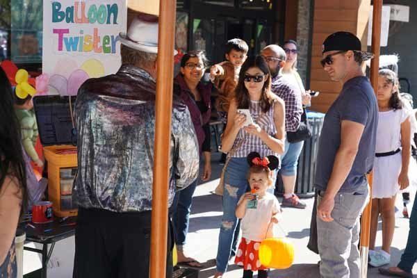 A group of people are standing around a balloon twister stand.