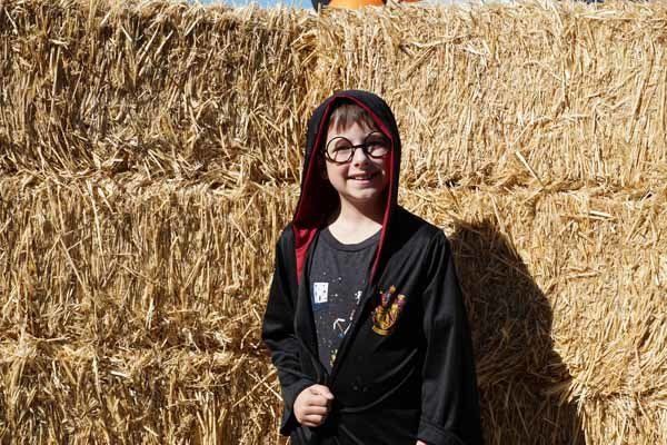 A young boy in a harry potter costume is standing in front of a hay bale.