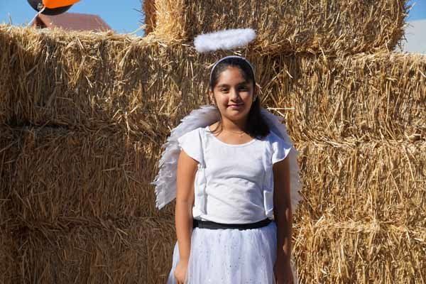 A girl dressed as an angel is standing in front of hay bales