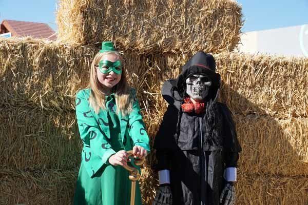 A girl in a green dress is standing next to a boy in a black costume.