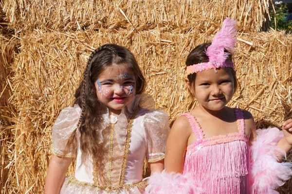 Two little girls are posing for a picture in front of a hay bale.