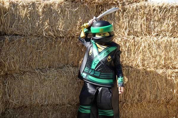 A child in a lego ninjago costume is standing in front of a pile of hay.