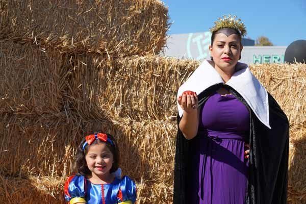 A woman in a purple dress is standing next to a little girl in a snow white costume.