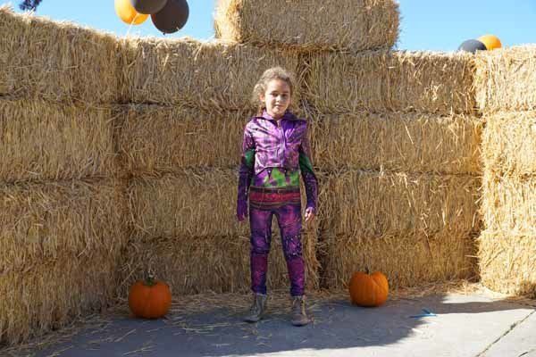 A little girl is standing in front of hay bales and pumpkins.