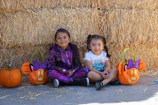 Two little girls are sitting next to each other in front of a hay bale.