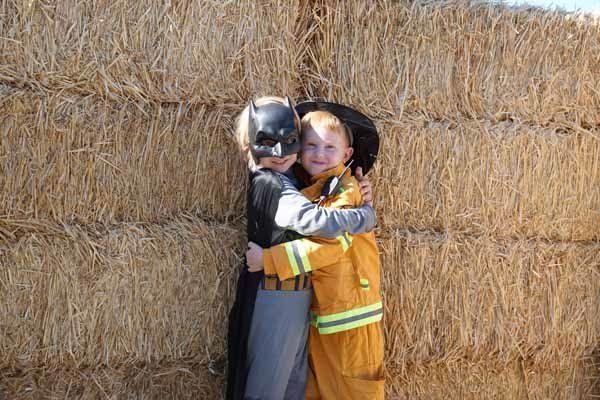 Two children in costumes are hugging each other in front of a hay bale.