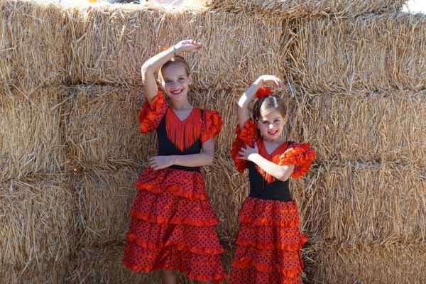 Two young girls in red dresses are standing in front of hay bales.