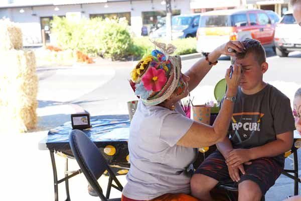A woman is applying makeup to a young boy 's face.
