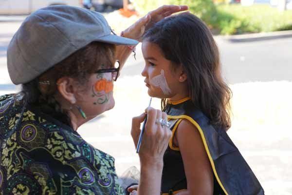 A woman is painting a little girl 's face with a brush.