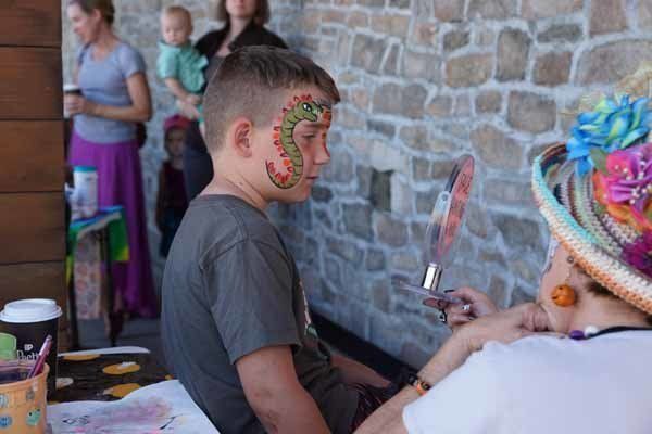 A young boy is getting his face painted by a woman.