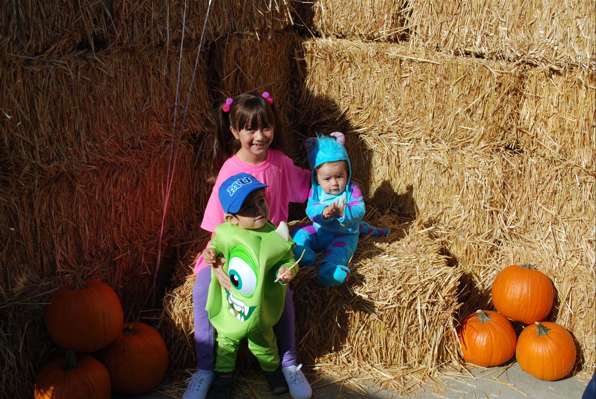Two children in monsters inc costumes are sitting on hay bales.