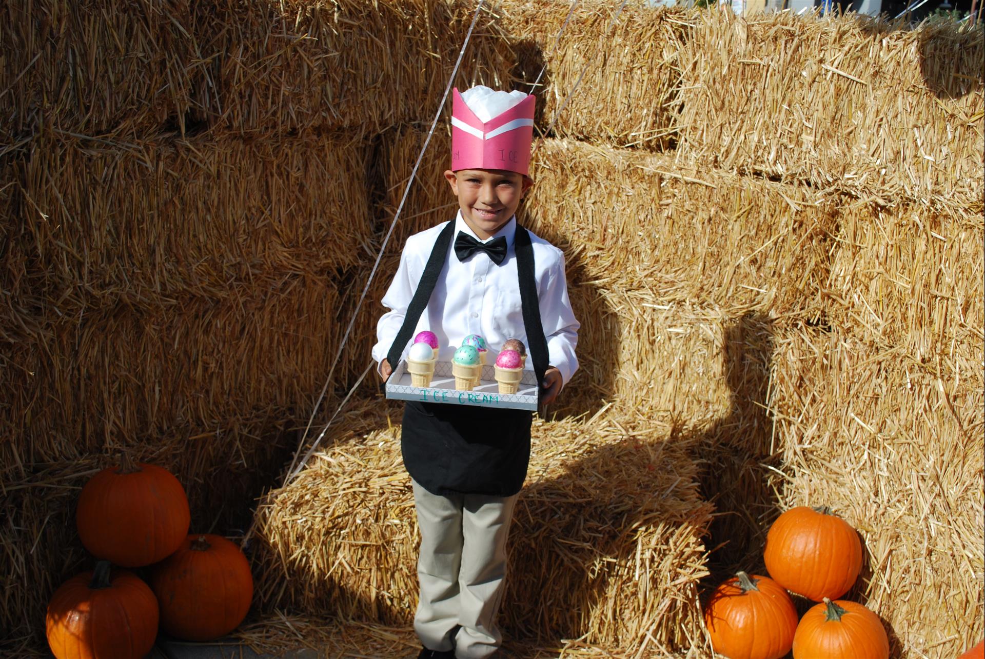 A little boy in a costume is holding a tray of ice cream cones.