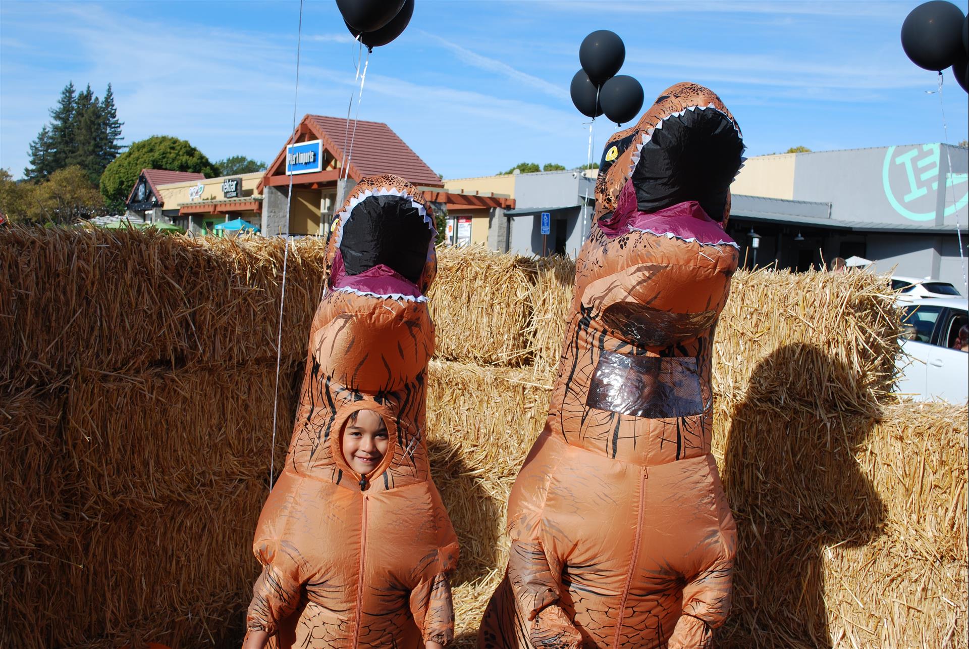 Two people dressed as dinosaurs are standing next to each other in front of hay bales.