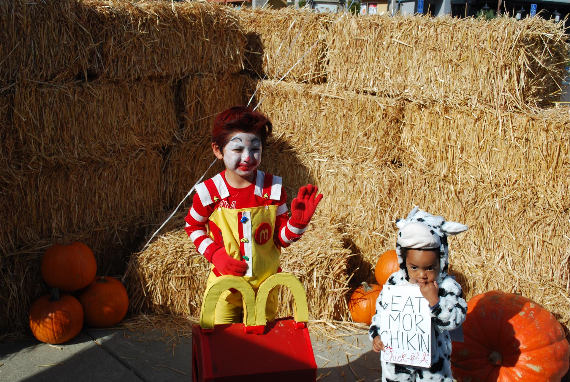 Two children dressed as mcdonald 's characters are standing in front of hay bales