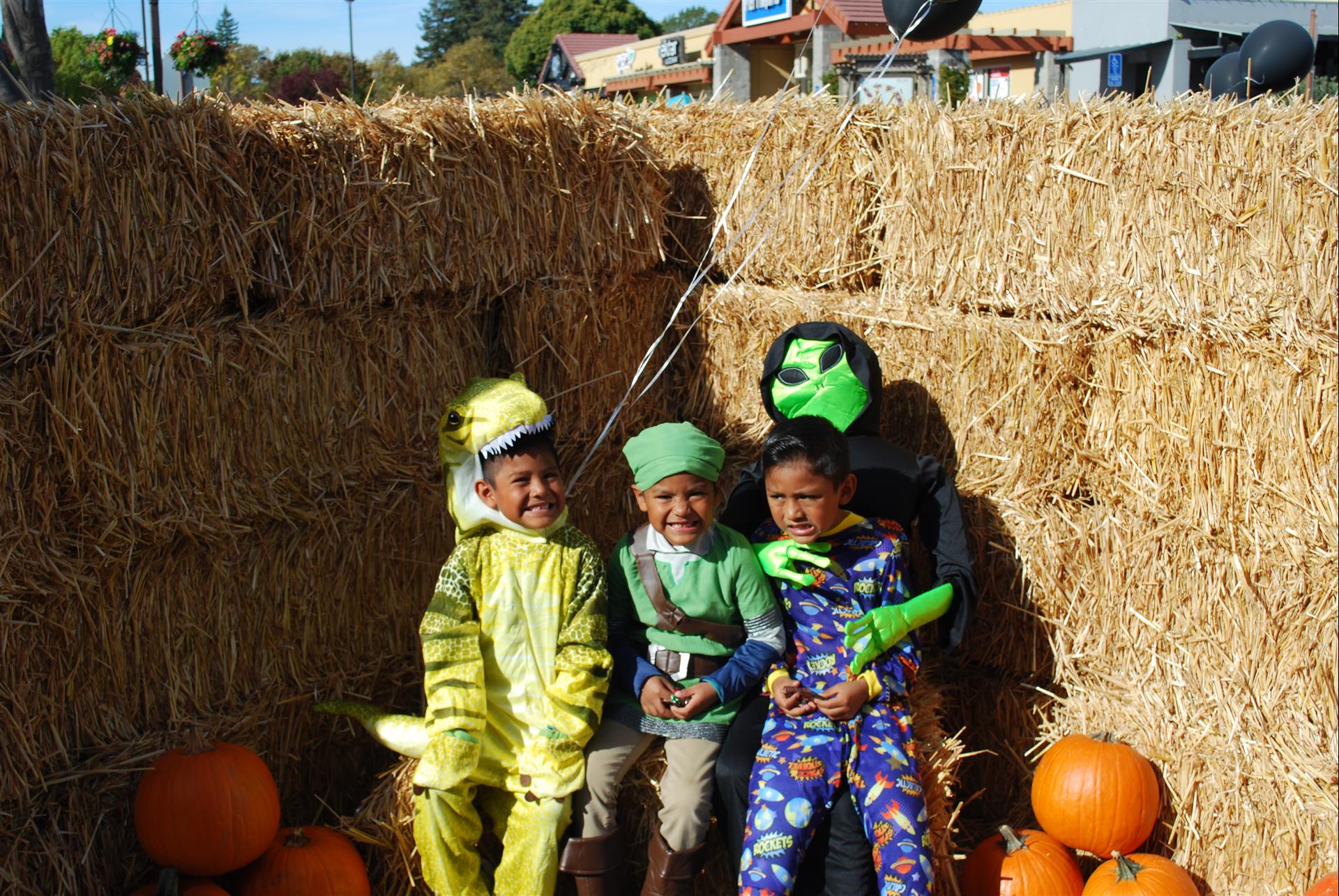 A group of children in costumes are posing for a picture in front of a hay bale.