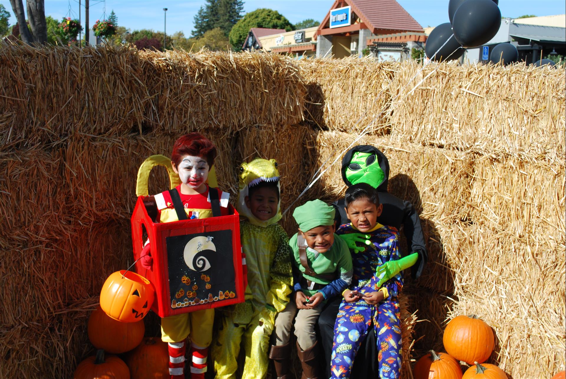 A group of children in halloween costumes are sitting on hay bales.