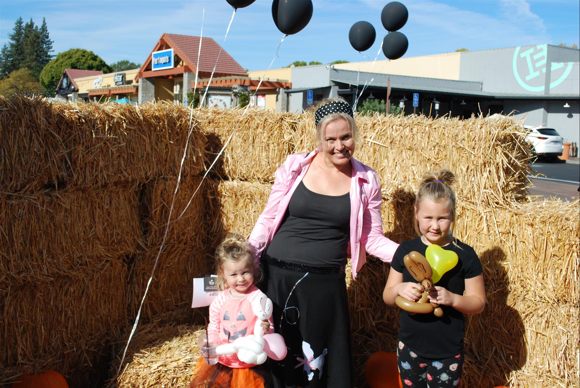 A woman and two little girls are posing for a picture in front of hay bales.