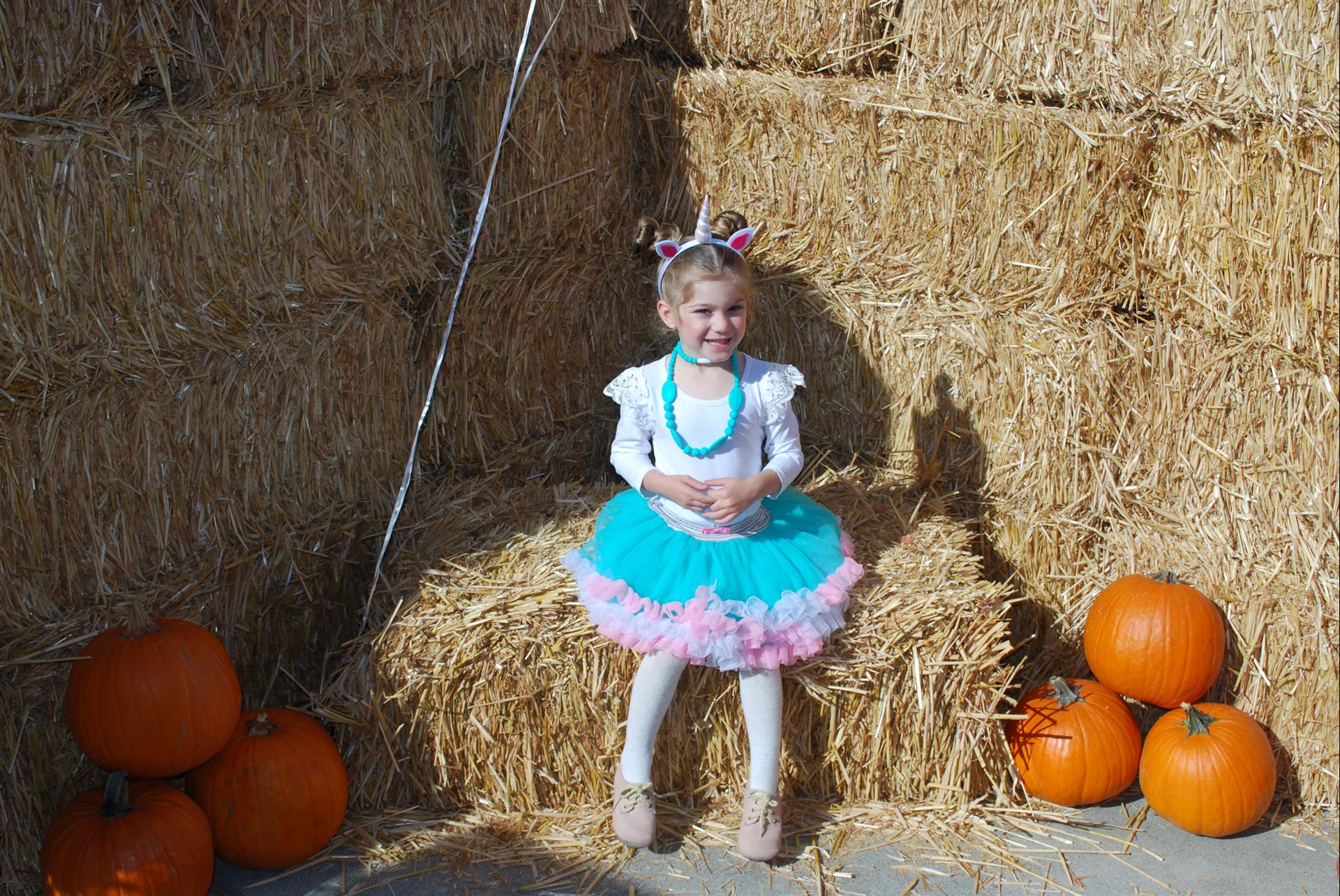A little girl is sitting on a bale of hay surrounded by pumpkins.