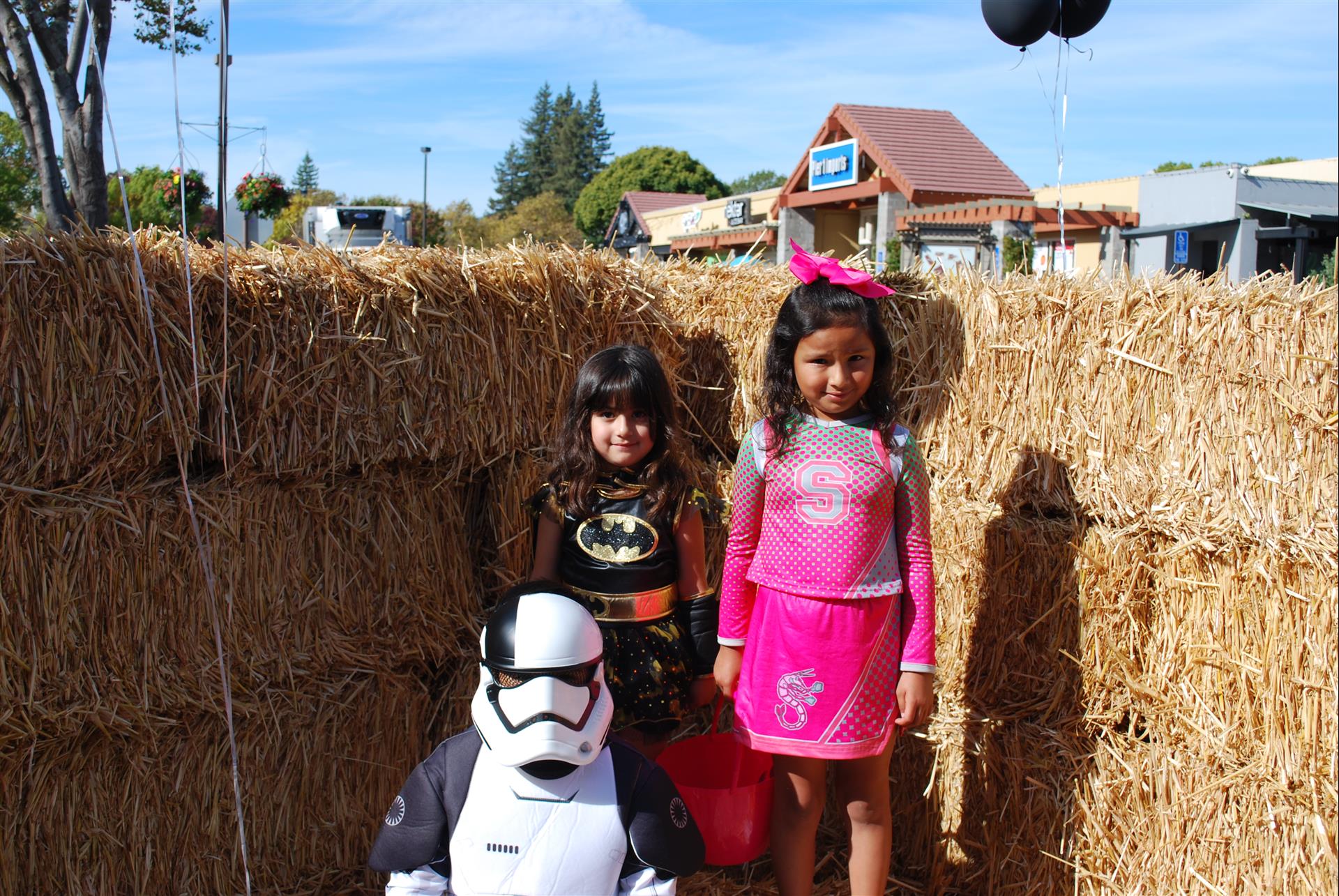 Two little girls and a storm trooper pose for a picture in front of hay bales.