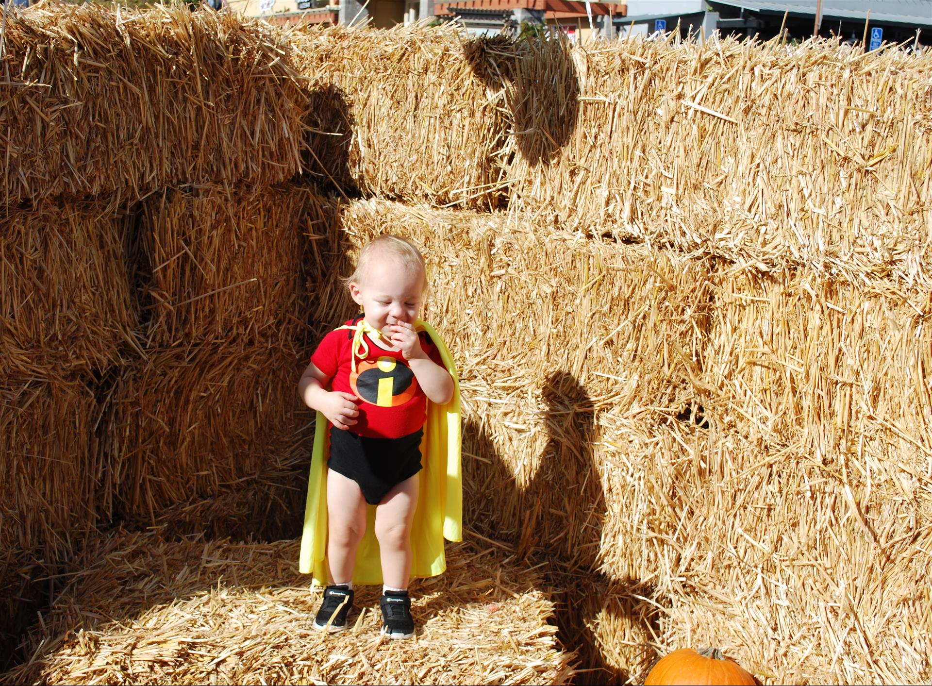 A baby in a superhero costume is standing in a pile of hay