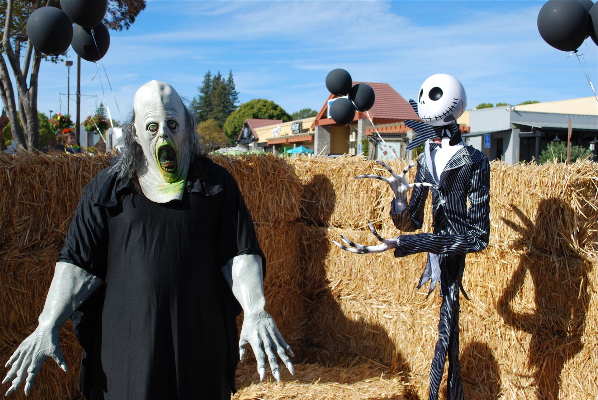A skeleton and a zombie are standing next to each other in front of hay bales