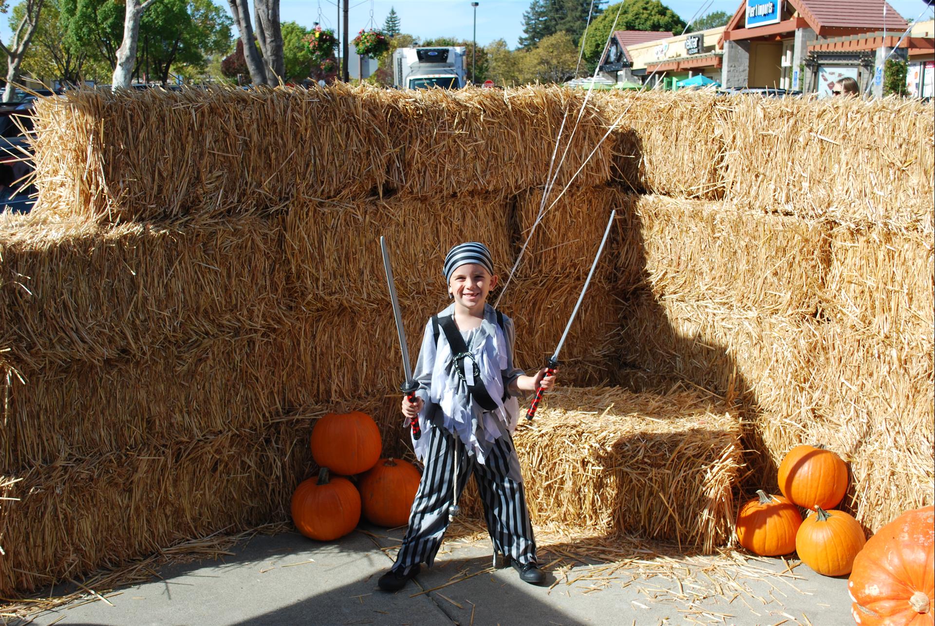 A boy in a pirate costume is standing in front of hay bales and pumpkins