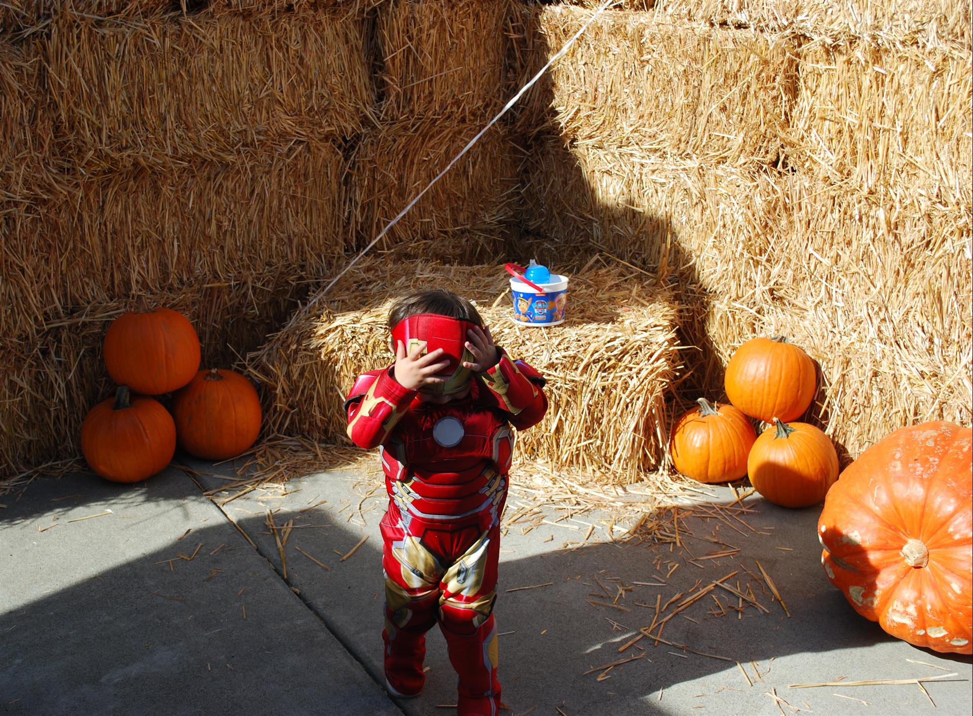 A child dressed as iron man is standing in front of hay bales and pumpkins