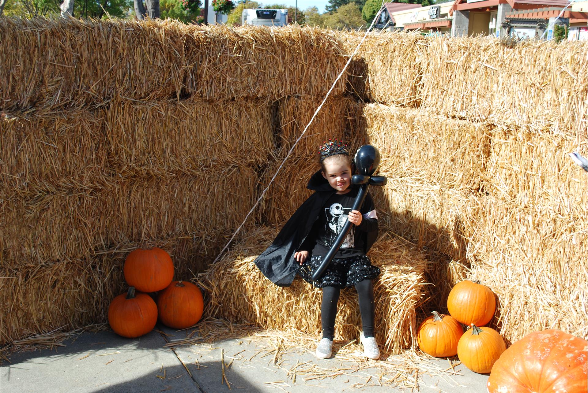 A little girl is sitting on a bale of hay holding a balloon.
