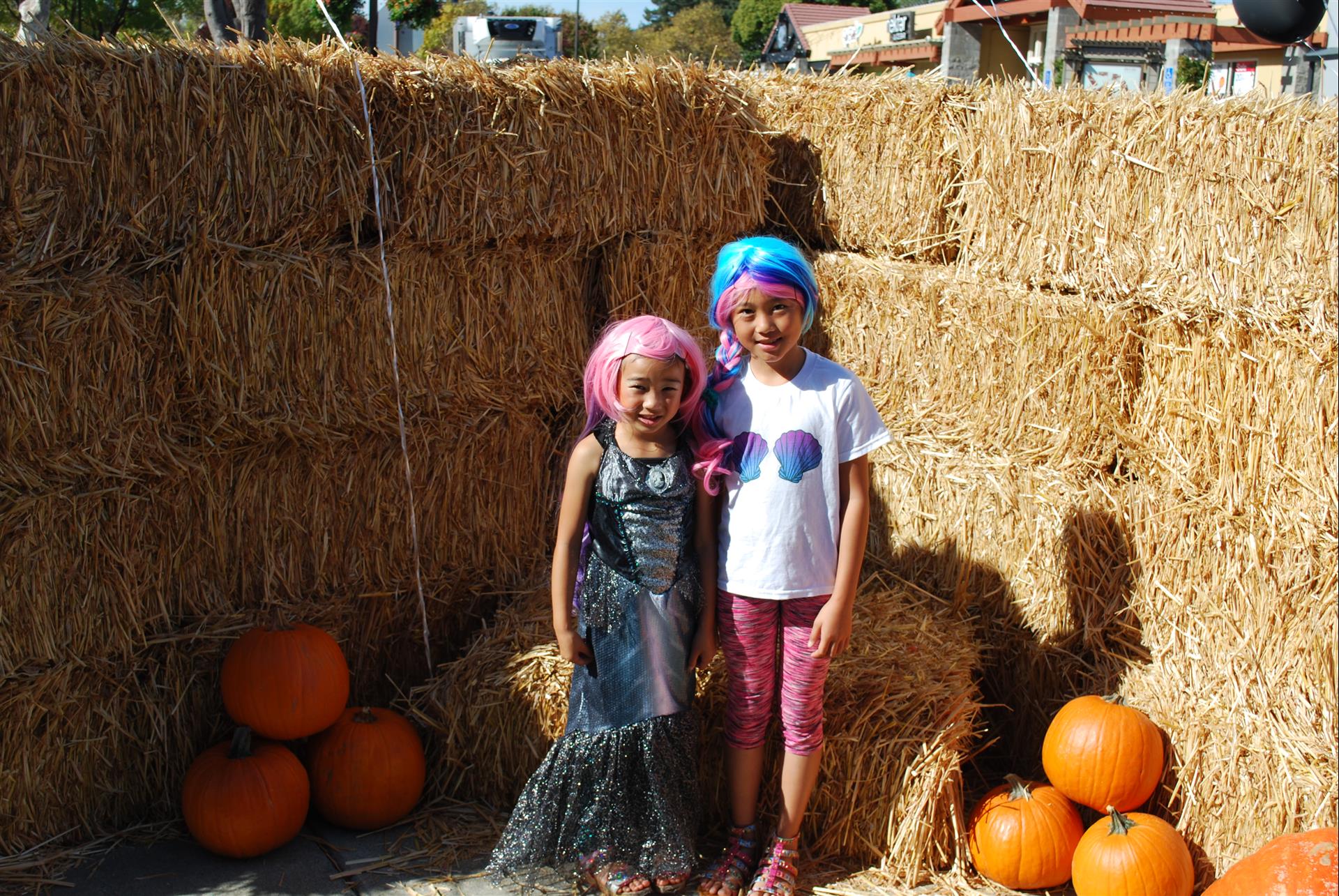Two little girls are posing for a picture in front of hay bales and pumpkins.