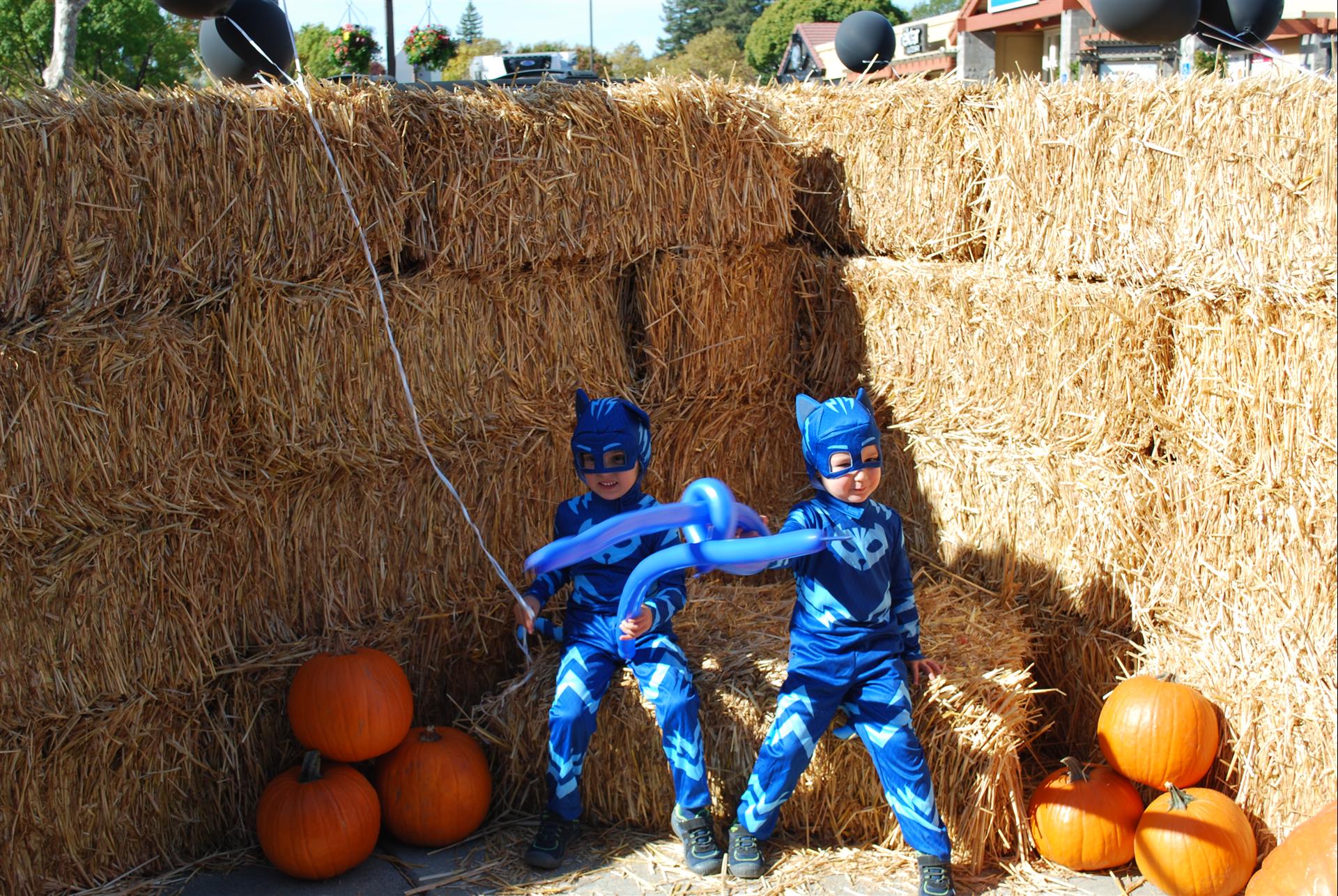 Two children in costumes are standing next to hay bales and pumpkins.