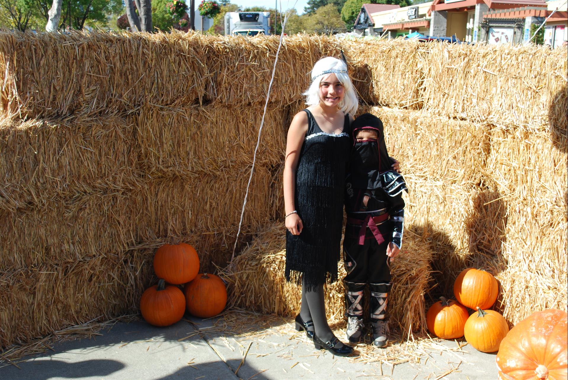 A woman and child are posing for a picture in front of hay bales and pumpkins