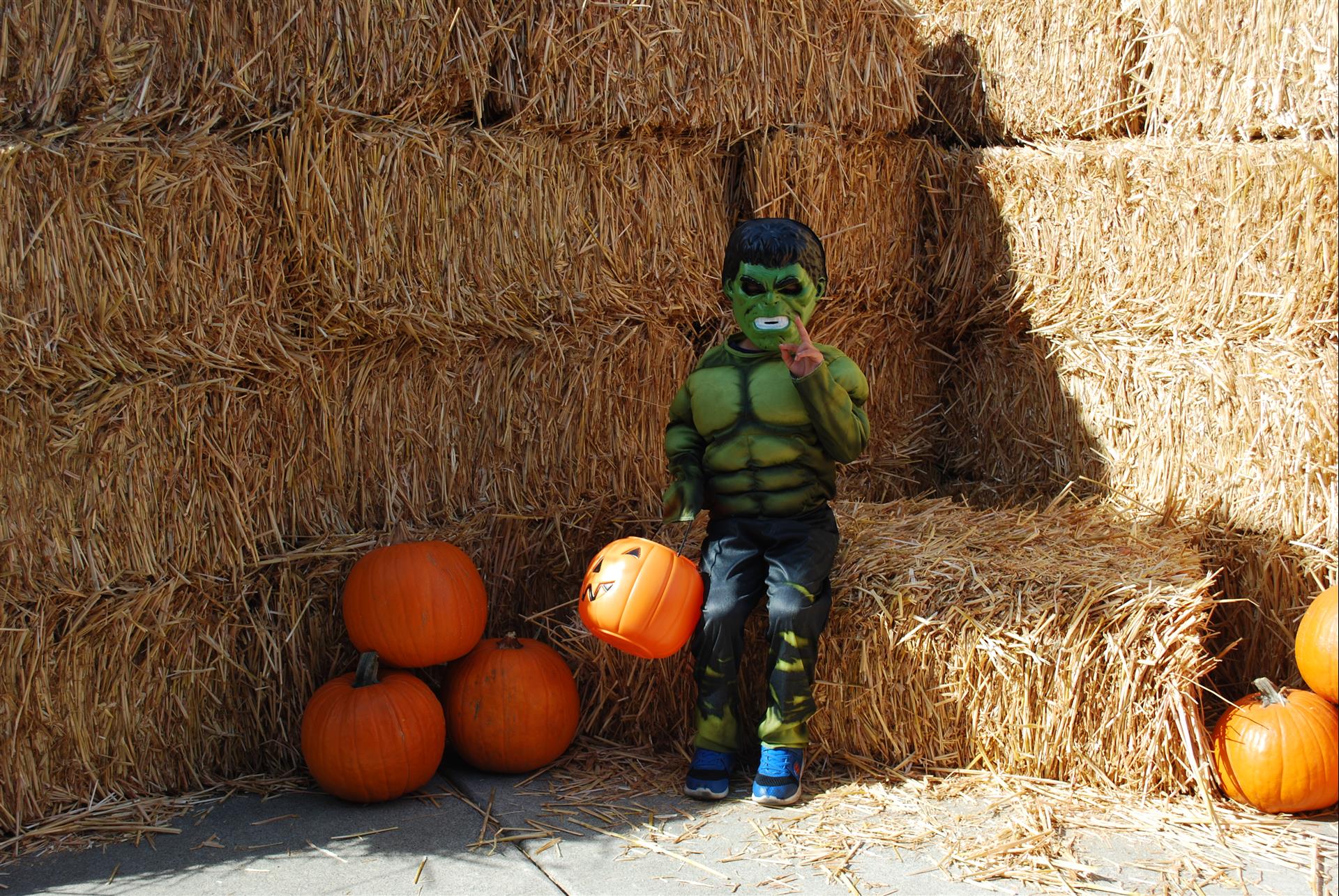 A child in a hulk costume is sitting on a bale of hay holding a pumpkin.