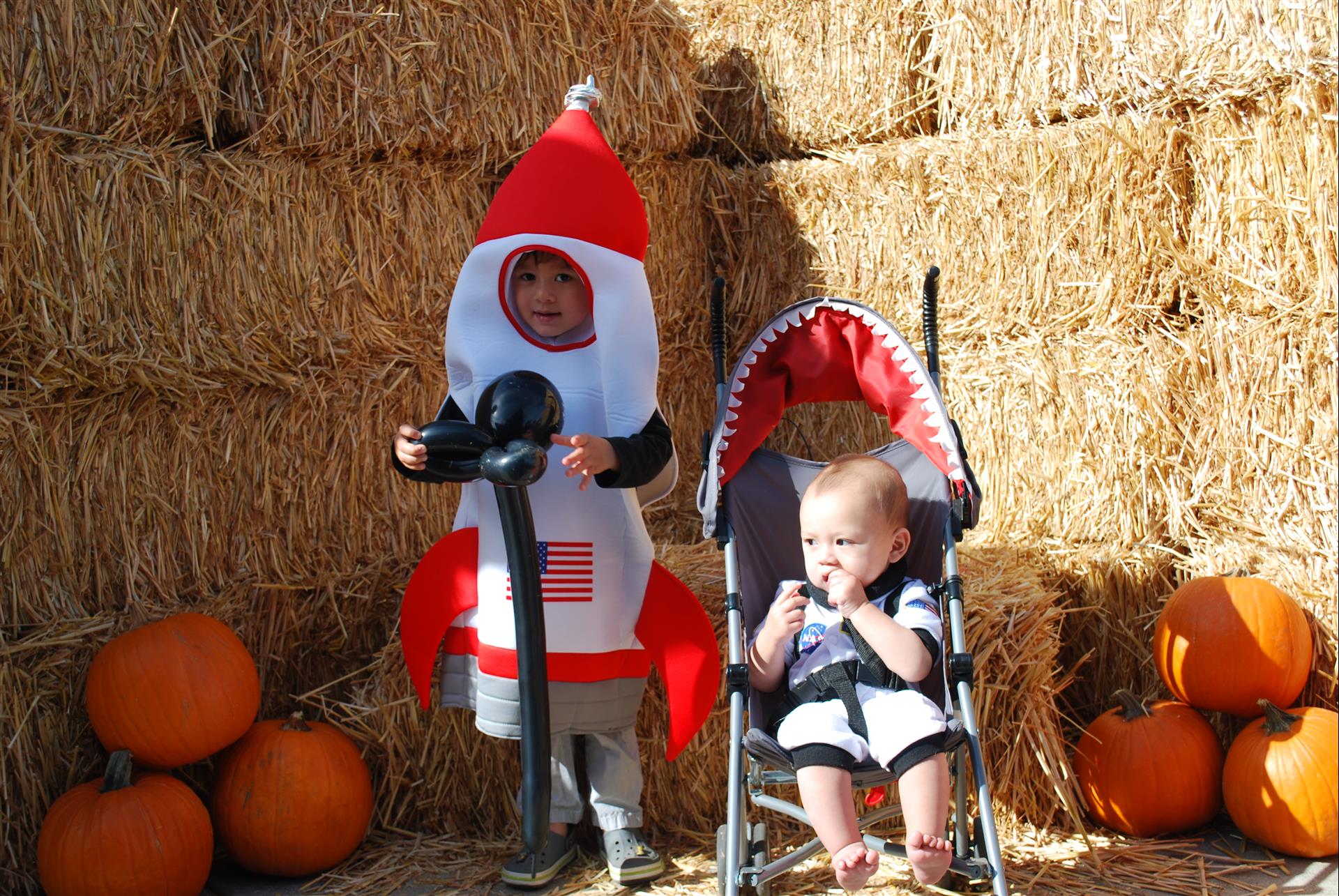 A child in a rocket costume is standing next to a baby in a stroller