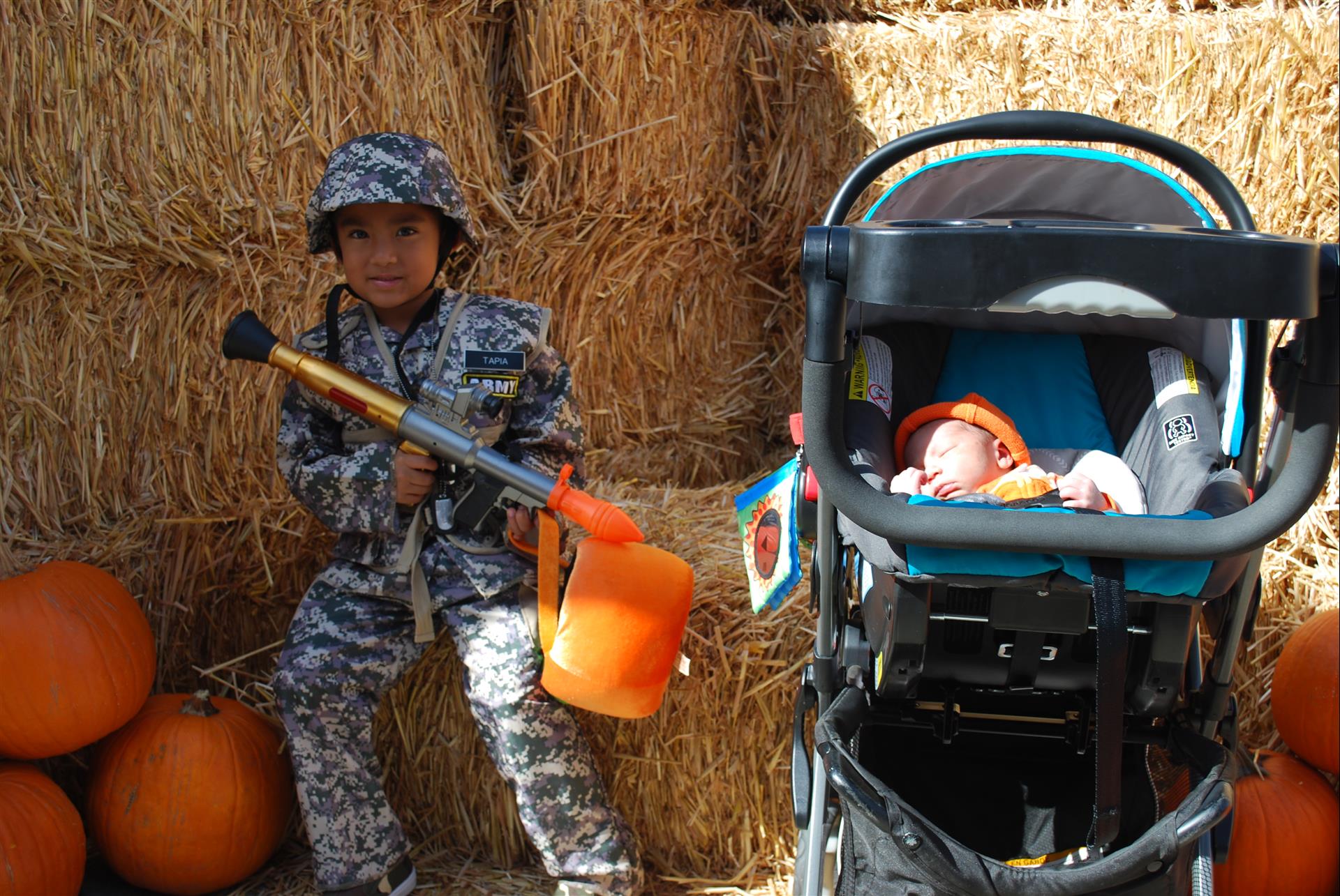 A baby in a stroller is sitting next to a boy in a soldier costume