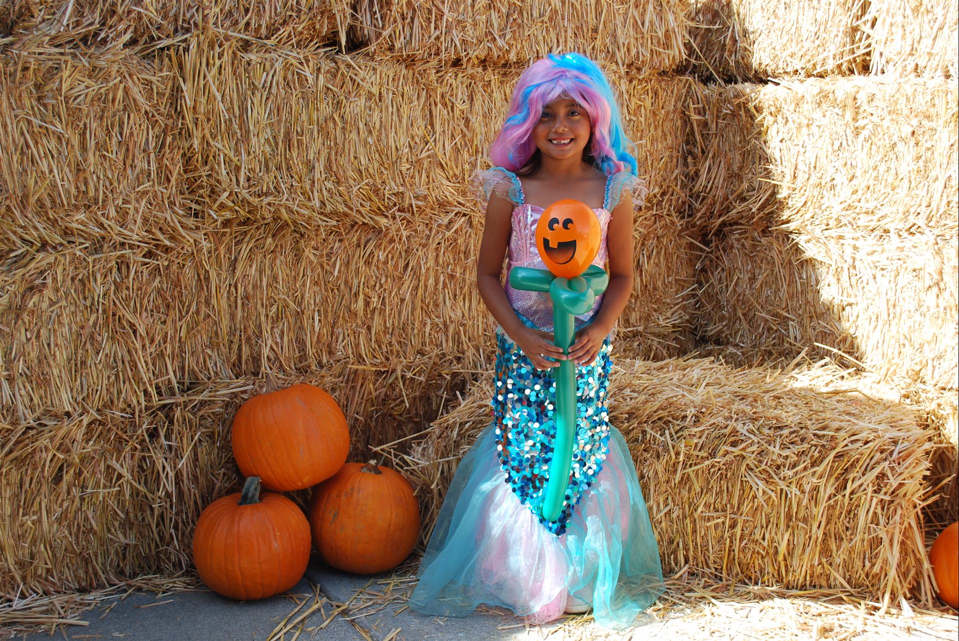 A little girl in a mermaid costume is holding a pumpkin.