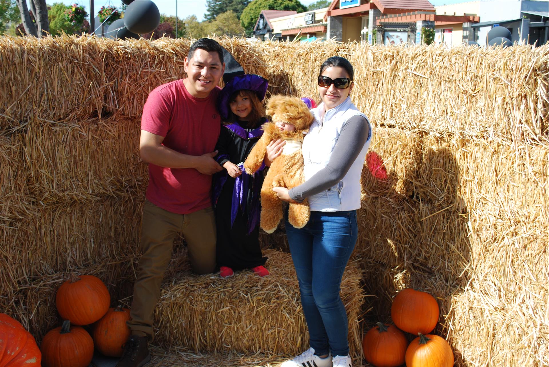 A family is posing for a picture in front of hay bales and pumpkins.