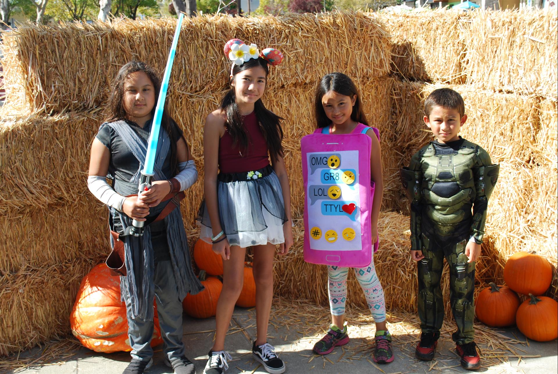A group of children in costumes are posing for a picture in front of hay bales.