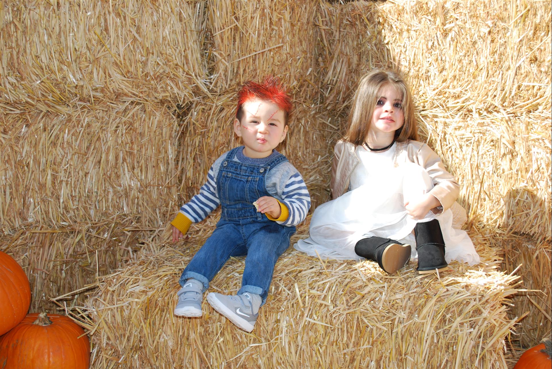 A boy and a girl are sitting on a bale of hay surrounded by pumpkins.