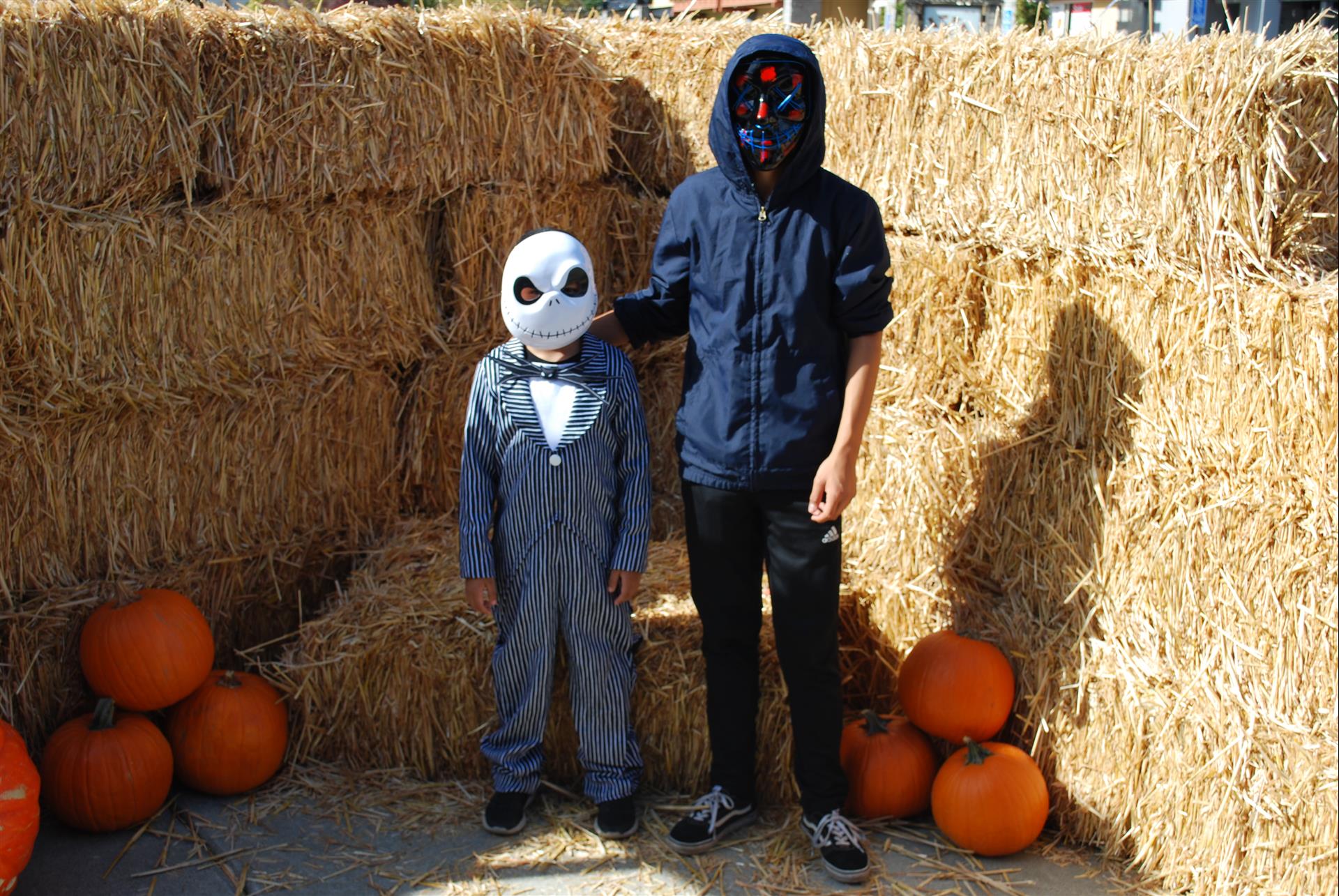 Two children in halloween costumes are standing next to hay bales and pumpkins.