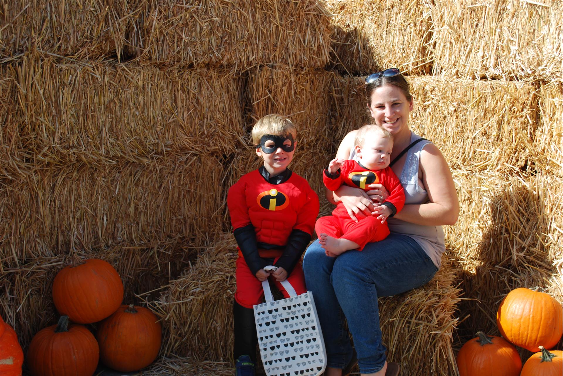 A woman is sitting on a hay bale with two children in costumes.