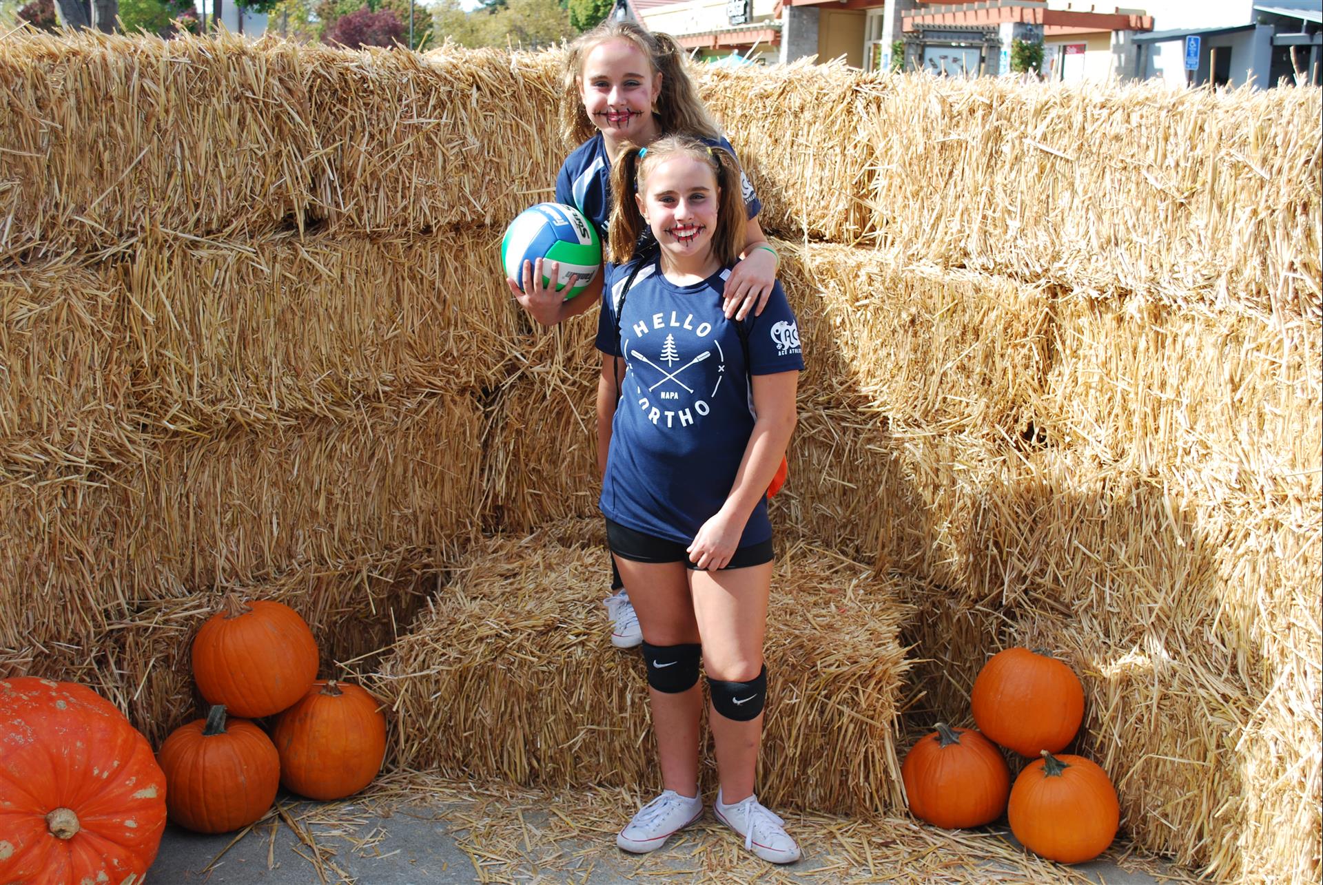 Two girls are posing for a picture in front of hay bales and pumpkins