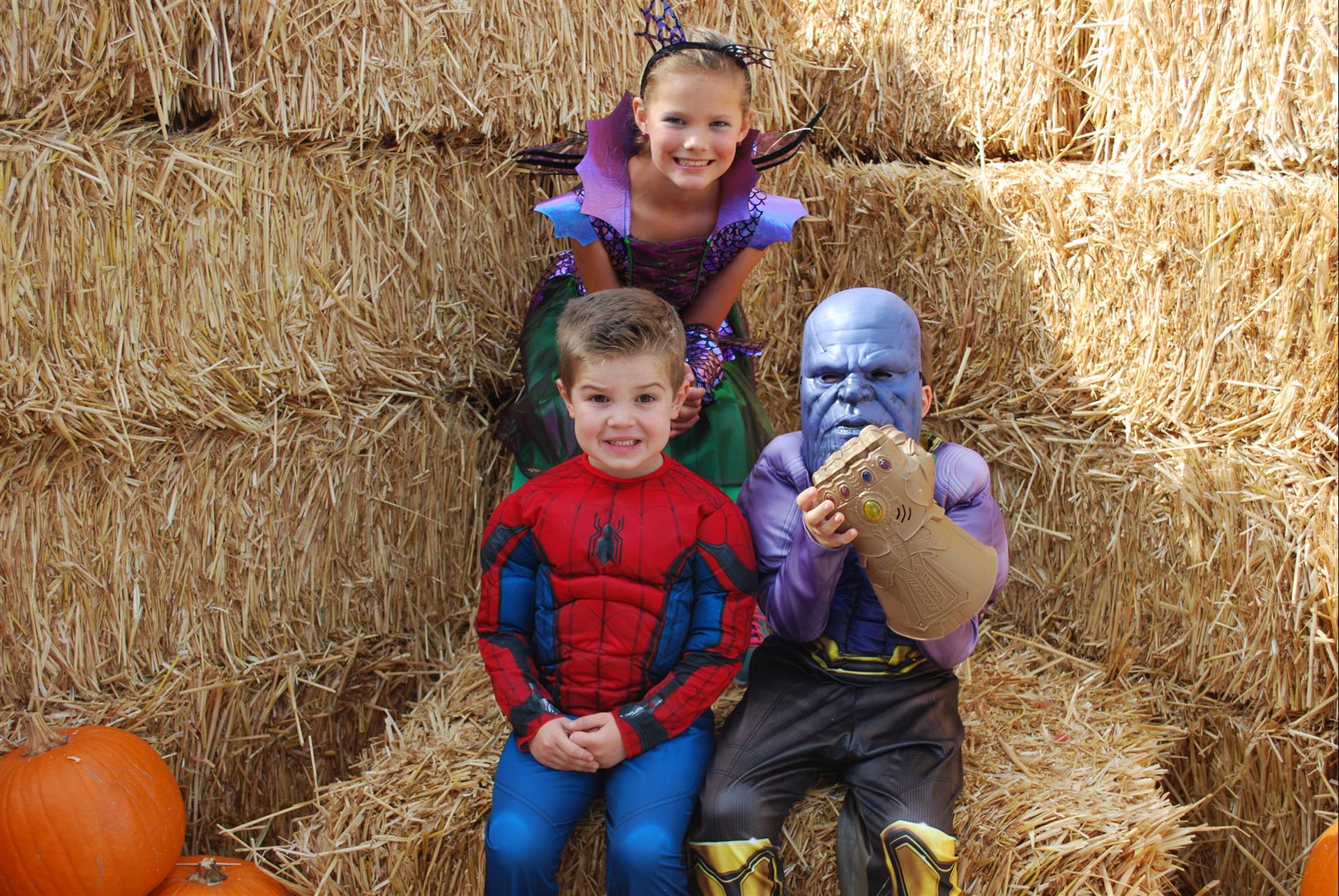 Three children dressed in costumes are sitting on bales of hay.
