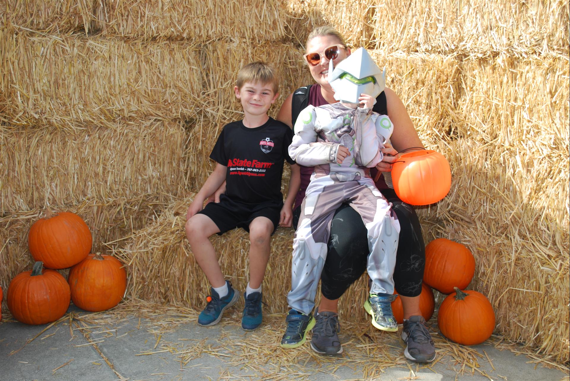 A woman and two children are sitting on a hay bale holding pumpkins.