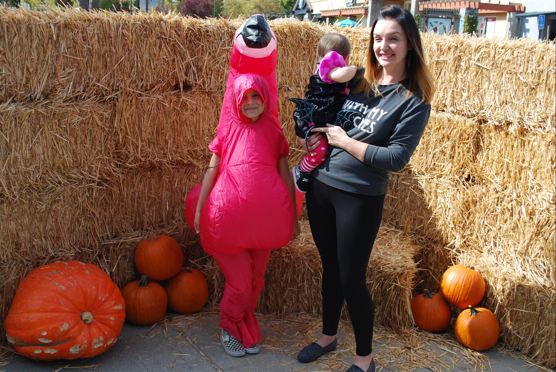 A woman is holding a baby and a child in a pink flamingo costume.