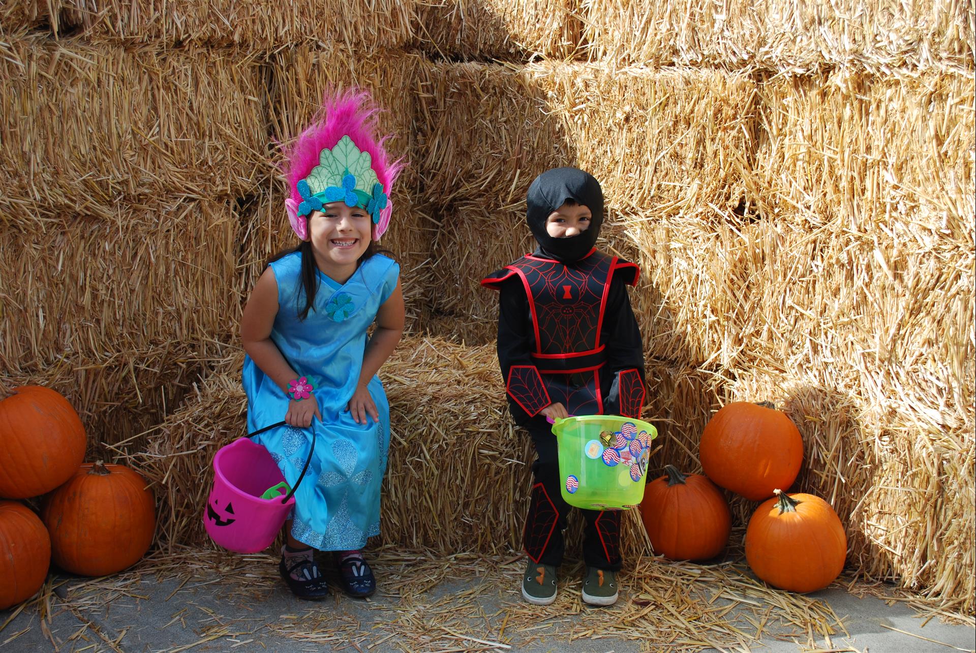 A girl in a troll costume is sitting next to a boy in a ninja costume.