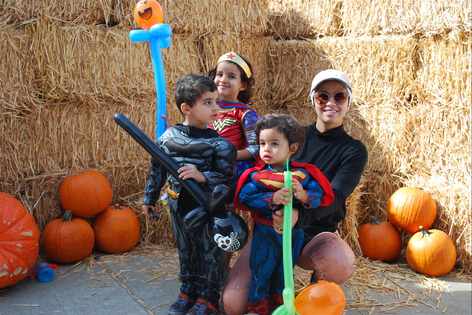 A woman is holding two children in costumes in front of pumpkins.